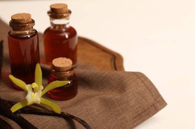 Aromatik vanilya özü, kapsüller ve çiçekler beyaz masada, yakın plan. Metin için boşluk