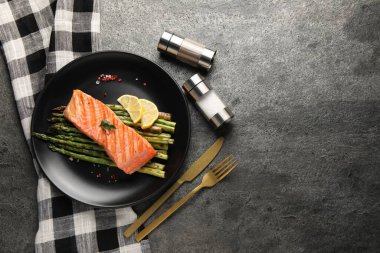 Gri masada servis edilen kuşkonmaz, limon ve baharatlı ızgara somon. Metin için boşluk