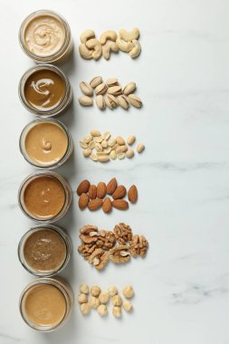 Kavanozlarda lezzetli fındık ezmesi ve beyaz mermer masada çiğ fındık, düz uzanmış