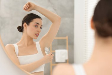 Güzel bir kadın banyoda aynanın yanında deodorant sürüyor.