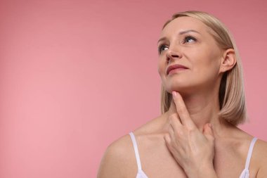 Güzel bir kadın pembe arka planda boynuna dokunuyor. Metin için boşluk