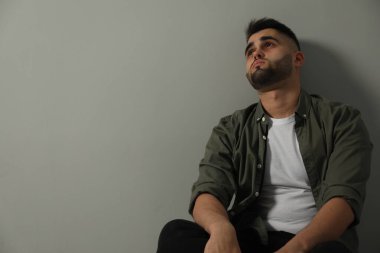 Üzgün adam açık gri duvarın yanında oturuyor. Metin için boşluk