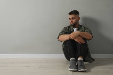 Açık gri duvarın yanında yerde oturan üzgün adam. Metin için boşluk