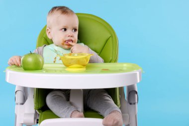 Küçük şirin bebek, yüksek sandalyede sağlıklı yiyecekler yiyor açık mavi arka planda, mesaj için yer var.