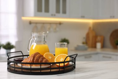 Kahvaltı mutfakta servis edilir. Taze kruvasan, reçel ve portakal suyu dolu tepsi beyaz masa, mesaj için yer