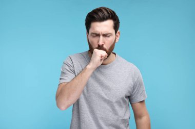 Açık mavi arka planda öksüren hasta bir adam. Soğuk belirtileri