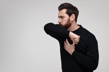 Hasta adam dirseğine doğru açık gri arka planda öksürüyor, mesaj için yer var. Soğuk belirtileri