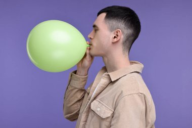 Mor arka planda açık yeşil balon şişiren genç adam