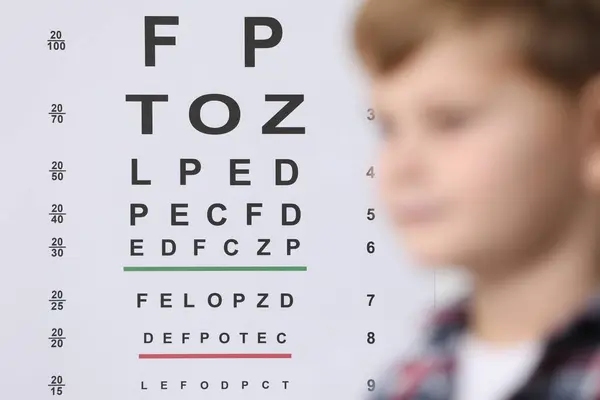 Cute little boy against vision test chart, selective focus