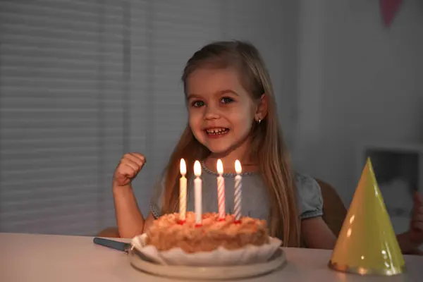 Cute girl with birthday cake at table indoors