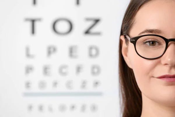 Young woman with glasses against vision test chart, closeup