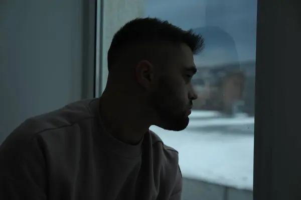 Sad man looking at window in dark room
