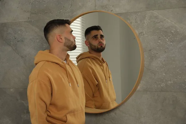 Sad young man near mirror at home