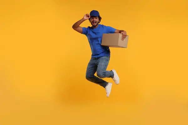 Happy courier with parcel jumping on orange background