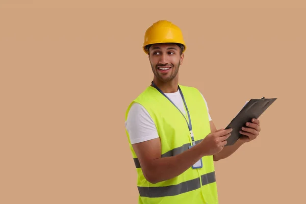 Engineer in hard hat holding clipboard on beige background, space for text