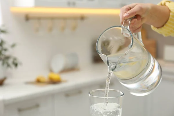 Woman pouring water from jug into glass in kitchen, closeup. Space for text