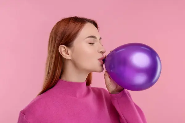 Woman inflating purple balloon on pink background