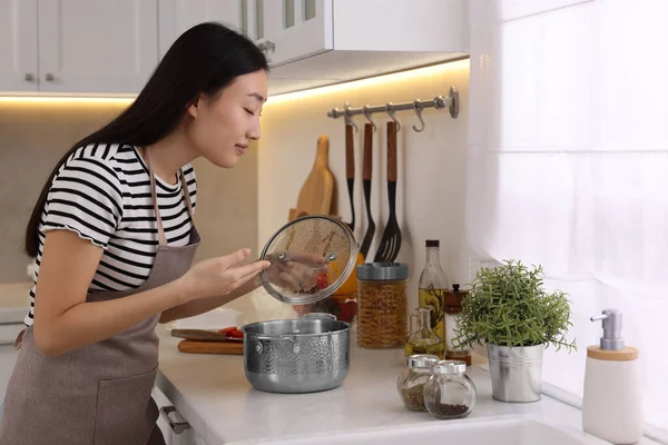 Beautiful woman smelling soup after cooking in kitchen