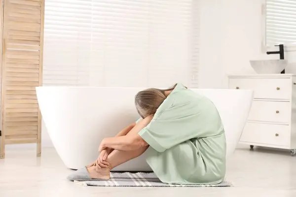 Menopause. Depressed woman near bath tub in bathroom