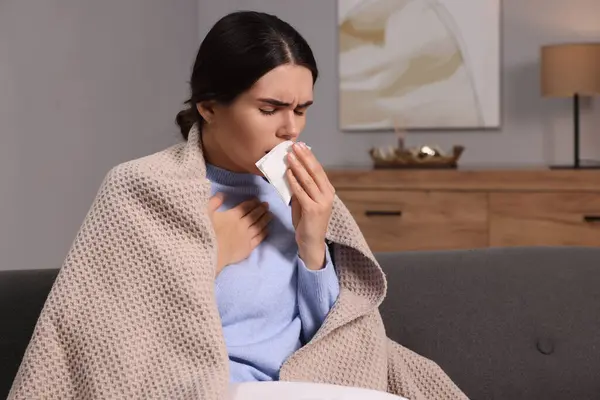 Woman coughing with tissue on sofa at home, space for text. Cold symptoms