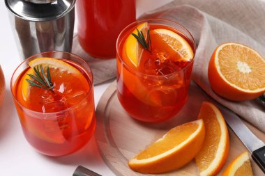 Aperol spritz kokteyli, biberiye ve portakal dilimleri beyaz ahşap masada.