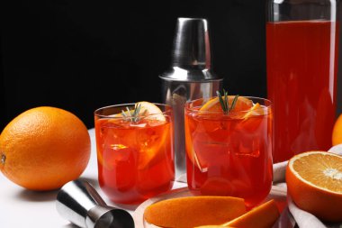 Aperol sprey kokteyli, biberiye ve portakal dilimleri beyaz masada.