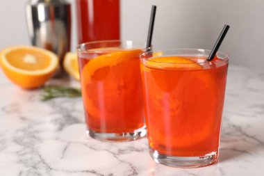 Aperol spritz kokteyli, portakal dilimleri ve pipetler beyaz mermer masada, yakın plan.