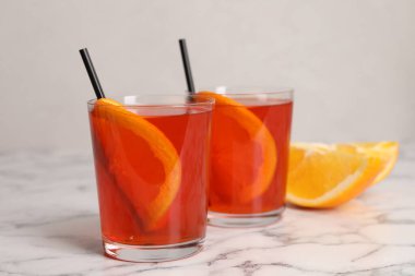 Aperol spritz kokteyli, portakal dilimleri ve beyaz mermer masa üzerinde pipetler.