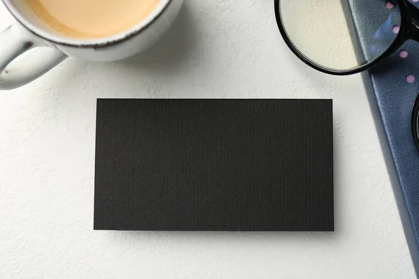 Blank black business card, cup of coffee, glasses and stationery on white table, top view. Mockup for design