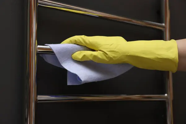 Woman cleaning heated towel rail with rag, closeup