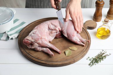 Beyaz ahşap masada bütün tavşanı kesen kadın, yakın plan.