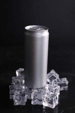 Alüminyum kutu enerji içeceği ve buz küpleri siyah masada.