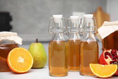 Cam şişelerde mayalanmış kombu çayı ve mutfakta beyaz masada taze meyve.