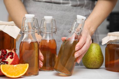 Beyaz masada mayalanmış kombu çayı şişelerini alan kadın, yakın plan.