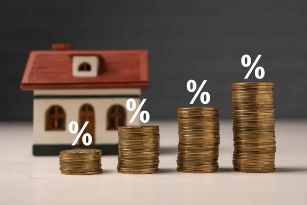 Mortgage rate. Stacked coins, percent signs and model of house