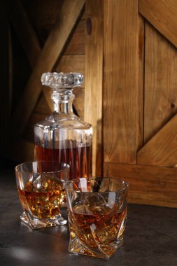 Buzlu viski bardakta ve gri masada şişe.