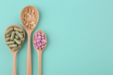 Tahta kaşıklardaki farklı vitamin hapları turkuaz arka planda, düz yerde. Metin için boşluk