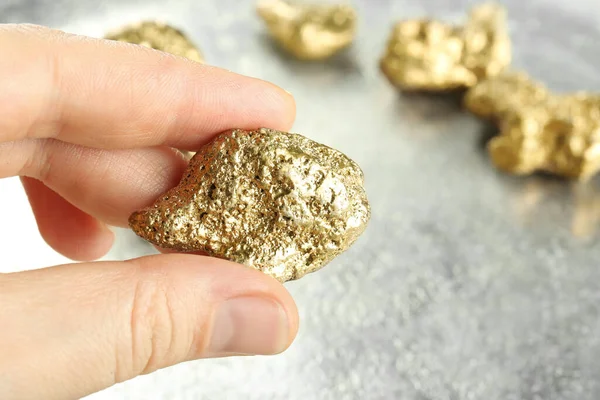 Woman holding gold nugget at light grey table, closeup. Space for text