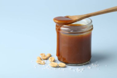 Tuzlu karamelli kavanoz, açık mavi arka planda kaşık ve fıstık, yakın plan. Metin için boşluk