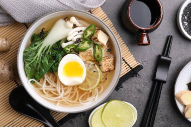 Bir kase vejetaryen ramen, soya sosu, kaşık ve çubuklar gri masada, düz yerde.