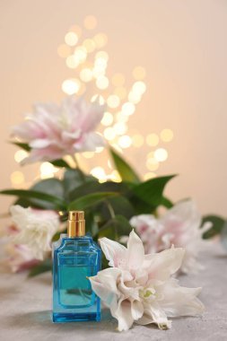Bir şişe parfüm ve güzel zambak çiçekleri bej arka planda bulanık ışıklarla, yakın plan