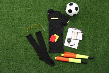 Üniforma, futbol topu ve yeşil çimlerin üzerinde diğer hakem ekipmanları, düz konum