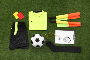 Üniforma, futbol topu ve yeşil çimlerin üzerinde diğer hakem ekipmanları, düz konum