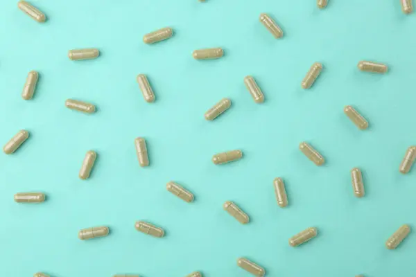 Many vitamin capsules on turquoise background, flat lay