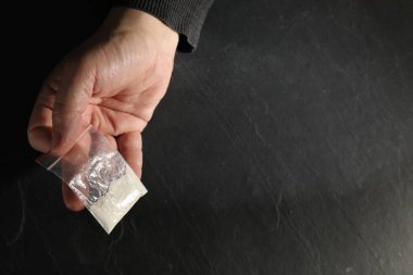 Gri dokuma masasında elinde plastik uyuşturucu torbası olan bağımlı bir adam. Metin için boşluk