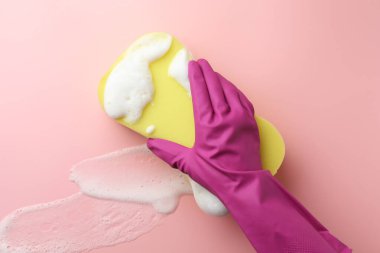 Lastik eldivenli temizleyici süngeri pembe arka planda tutuyor..