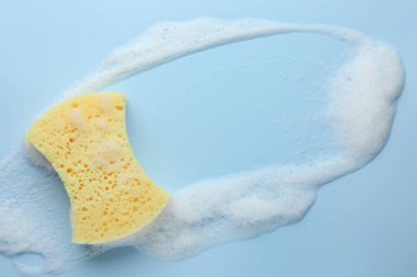 Açık mavi arka planda köpüklü sarı sünger, üst manzara. Metin için boşluk