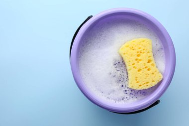 Açık mavi arka planda köpüklü ve süngerli kova, üst manzara. Metin için boşluk