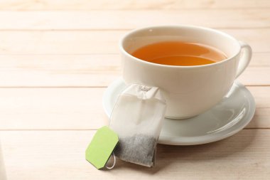 Hafif ahşap masada çay poşeti ve bir fincan sıcak içecek, yakın plan. Metin için boşluk