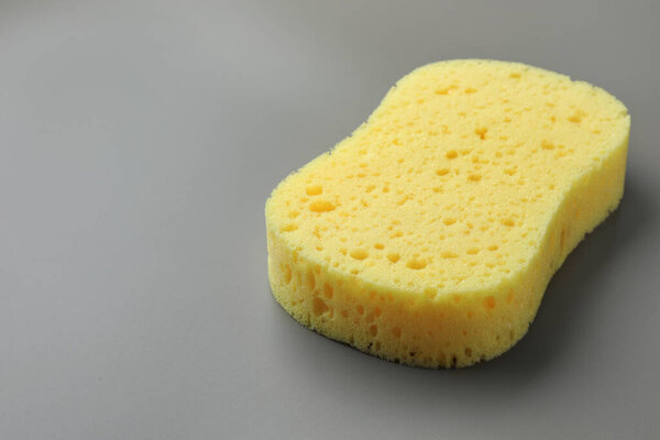 New yellow sponge on grey background, closeup. Space for text